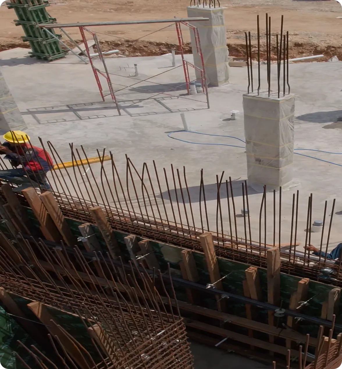 Construction site with reinforced concrete columns, exposed rebar, and workers preparing structural framework.